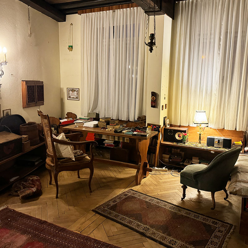 Vorher: Vollgestelltes Arbeitszimmer mit Schreibtisch und zahlreichen Kleingegenständen vor der systematischen Entrümpelung.